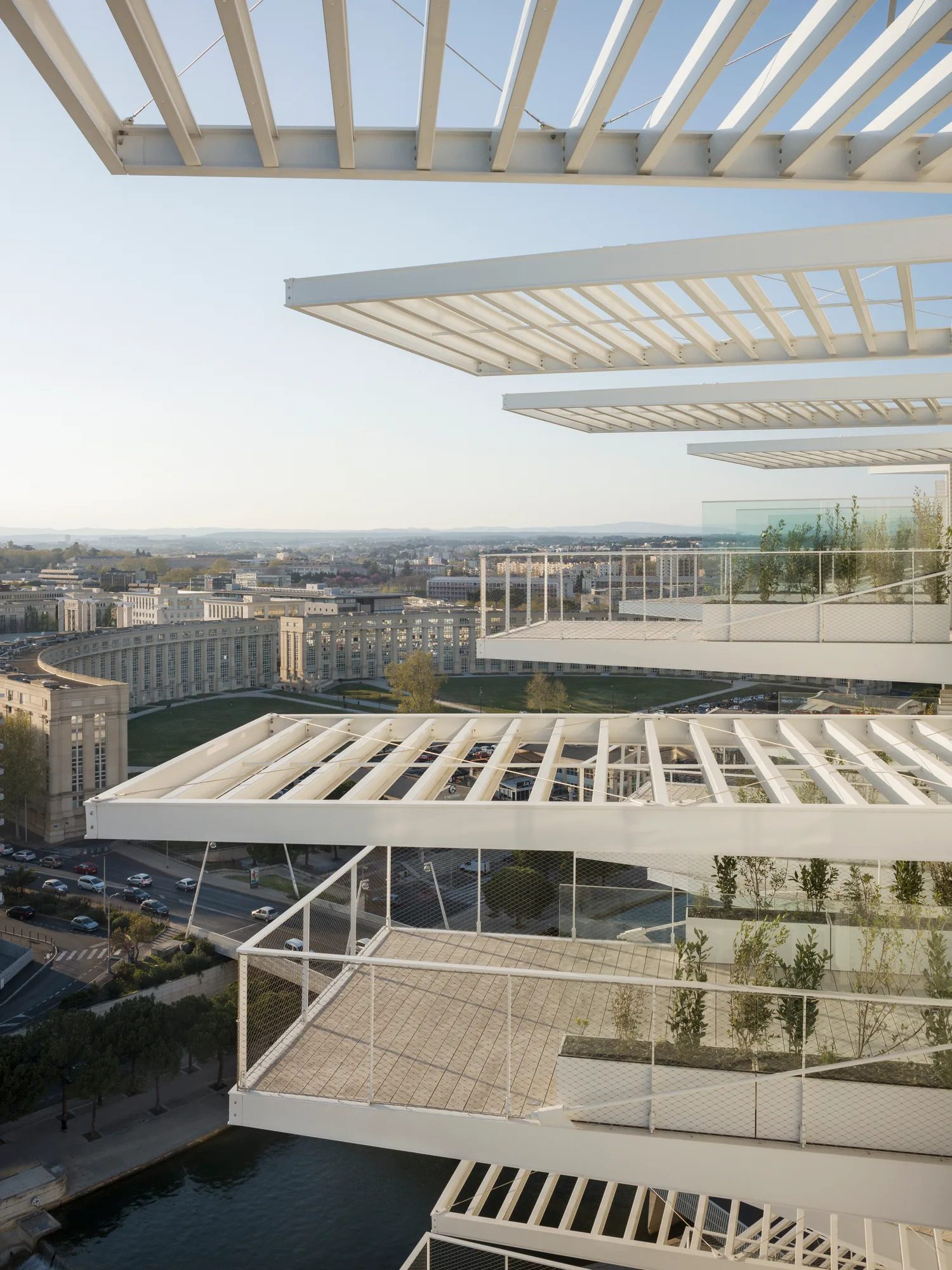 Depuis un balcon de l’Arbre Blanc : les brise-soleil à lames blanches des balcons du dessus se superposent au-dessus de la terrasse, et la ville de Montpellier s’étend jusqu’à l’horizon.