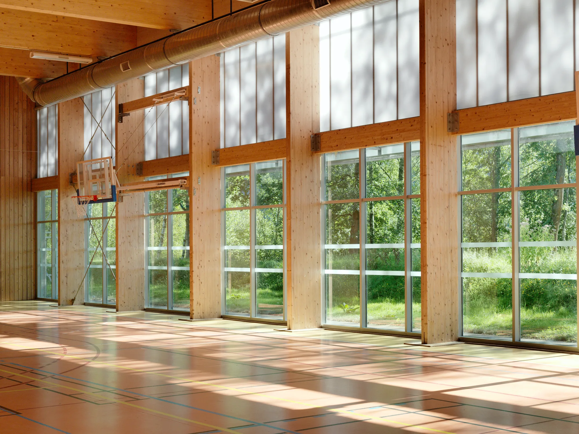 Le gymnase construit du lycée Jean Moulin à Revin : charpente et poteaux en bois lamellé-collé, hautes baies vitrées ouvertes sur la forêt.