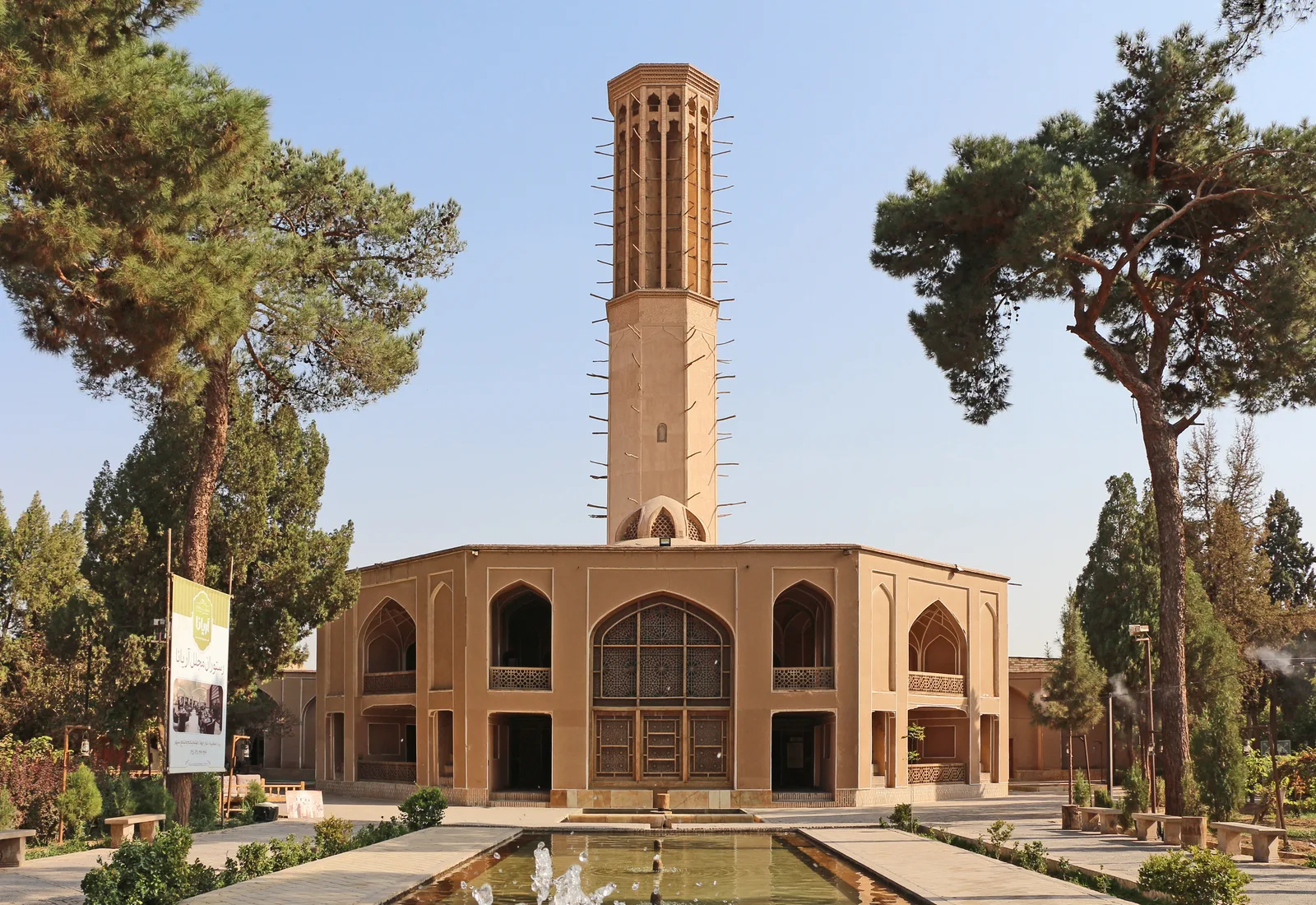 Pavillon du jardin de Dowlatabad à Yazd, surmonté d’une tour à vent octogonale d’une trentaine de mètres, devant un bassin.
