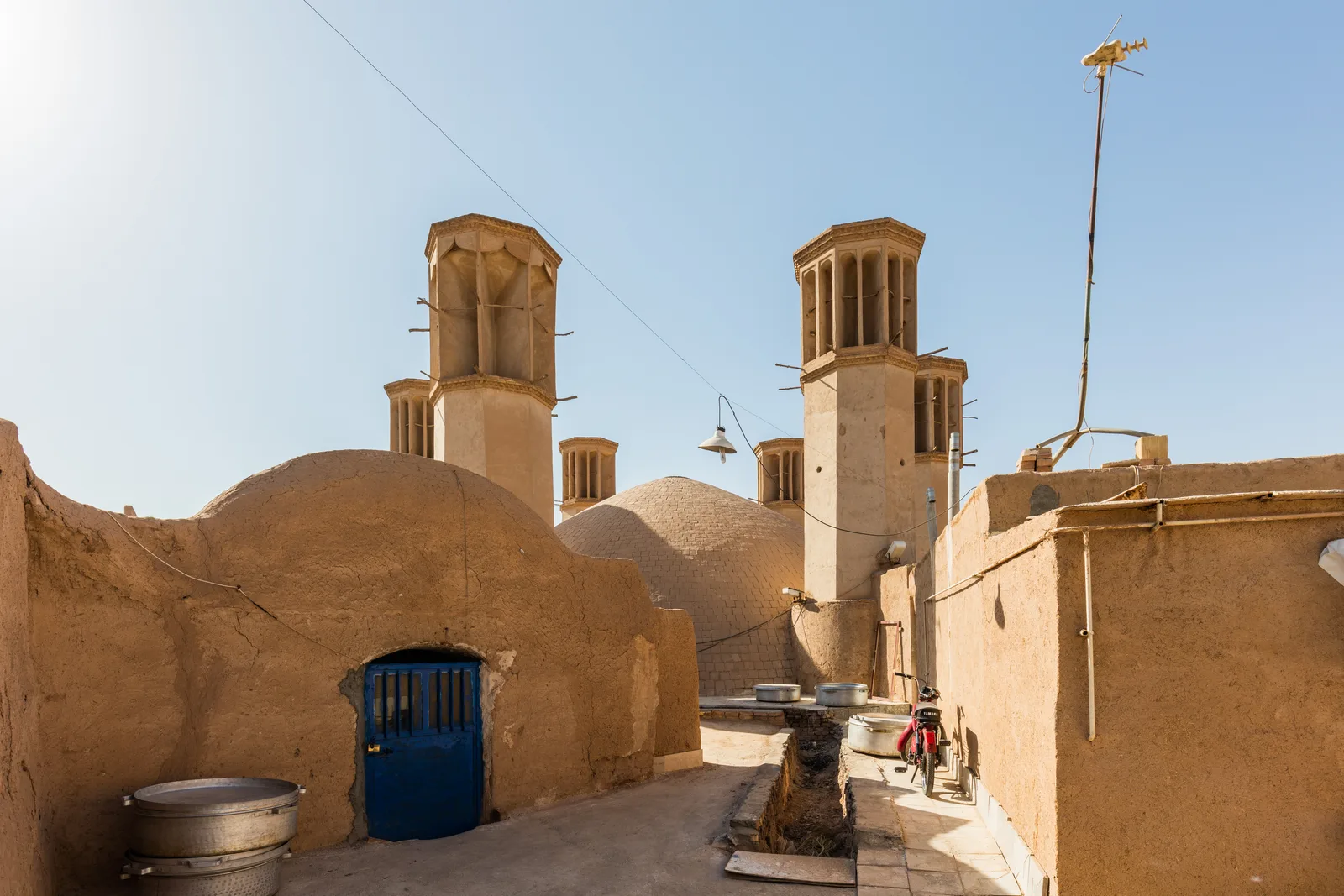 Six tours à vent de brique claire dressées au-dessus des toits en terrasse de la vieille ville de Yazd, en Iran, sous un ciel sans nuage.