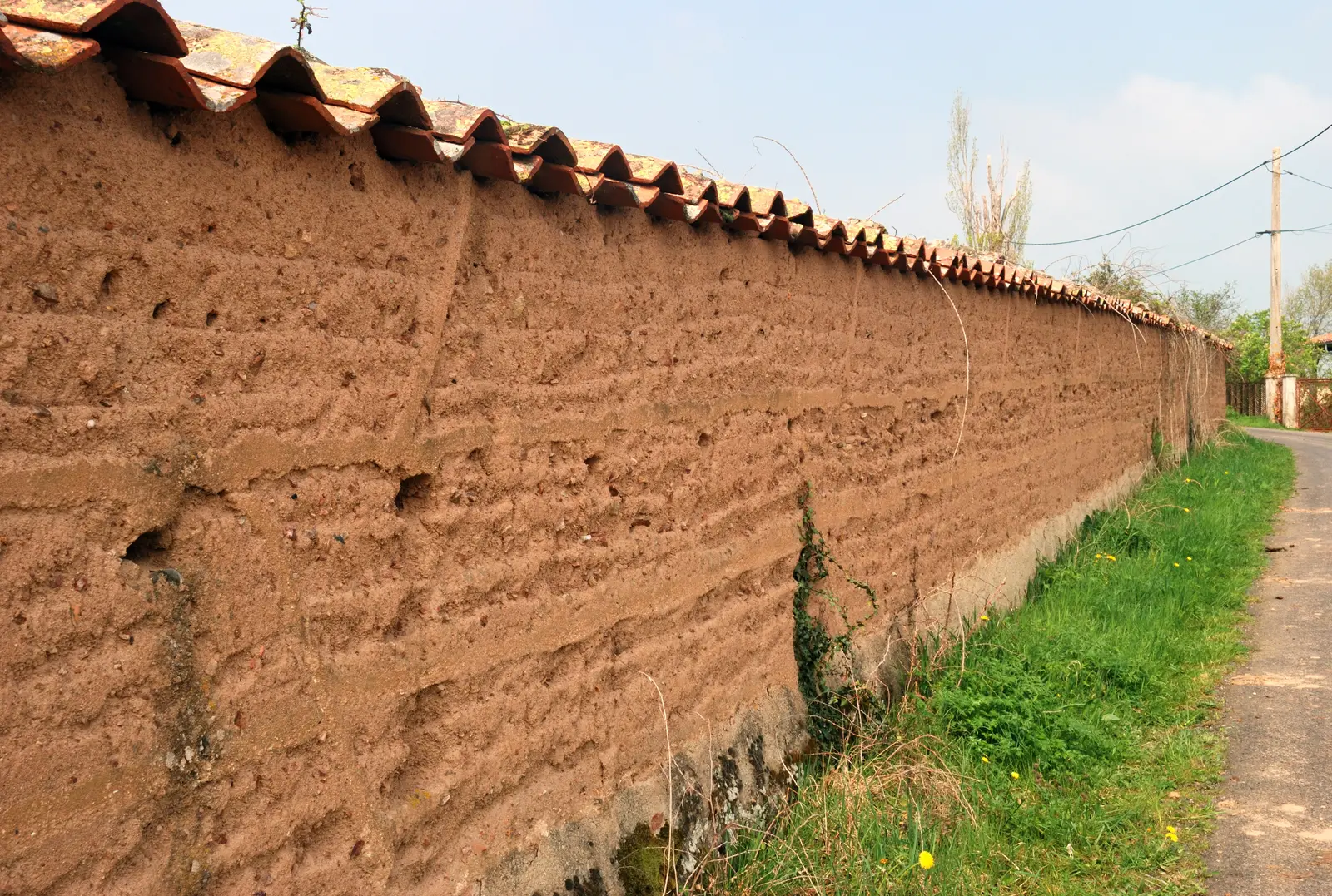 Détail rapproché d’un mur en pisé : lits de terre damée superposés, grains et cailloux visibles en surface.