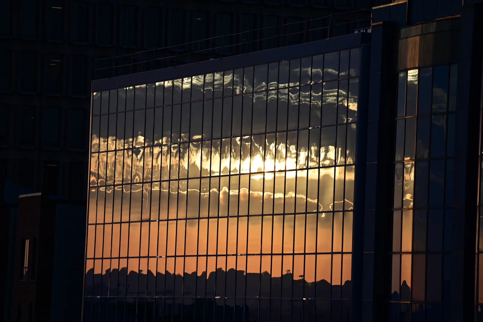 Mur-rideau entièrement vitré d’un immeuble de bureaux, dont les panneaux réfléchissent le lever de soleil en orange vif.